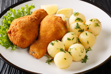 Delicious crispy deep-fried chicken served with lemon and boiled potatoes close-up in a plate on the table. horizontal