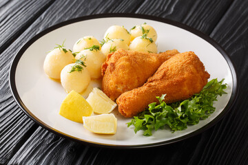 Austrian Fried Chicken Backhendl served with lemon and new potatoes close up in the plate on the table. Horizontal