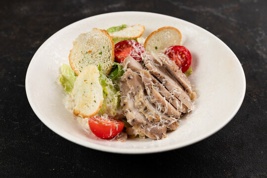 Caesar salad with chicken large frame on top in a white plate on a dark background, useful, delicious lunch or dinner