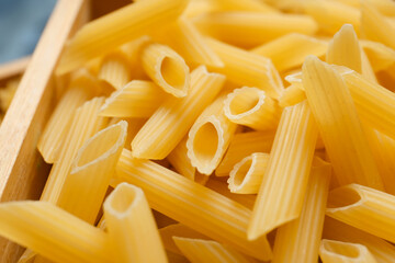 Uncooked penne pasta in wooden box