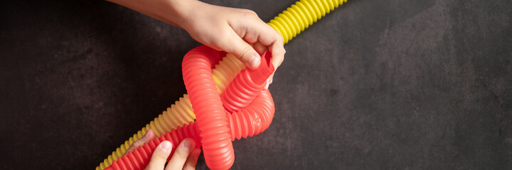 anti stress sensory pop tube toys in children's hands. little happy kids plays with a poptube toy on a black table. toddlers holding and playing pop tubes red and yellow bright color. banner