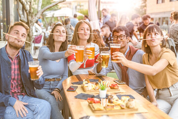 young university people having fun, group of friends eating food and drinking beer at restaurant, millennials outdoor leisure, warm filter and backlight sunset