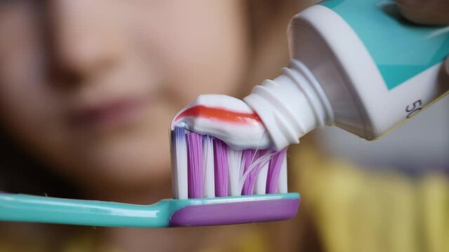 Little Girl Extruded Toothbrush With Bright Striped Toothpaste. Macro Shot Red and Blue Stripe Toothpaste Extruded Child Onto Toothbrush Closeup. Dental Health Oral Hygiene. Morning Teeth Brushing.