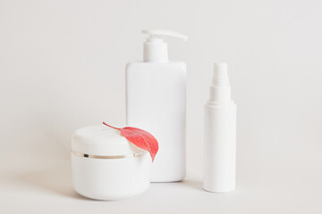 blank white bottles for cosmetics, mock up cream jar and red autumn fallen leaves on a beige light background