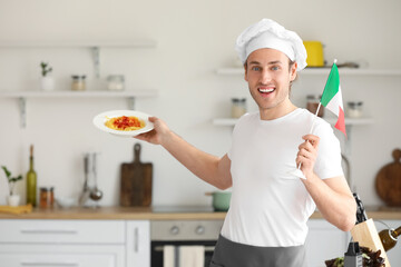 Handsome chef with tasty pasta and flag of Italy in kitchen