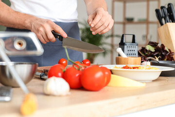 Male chef cutting fresh cherry tomato in kitchen, closeup