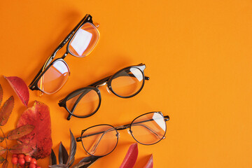 eye glasses nad red autumn leaves on orange background copy space