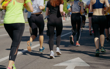 People in sportswear running on asphalt road, woman with colorful braids on foreground. Runners competing in city marathon. Healthy lifestyle. Concept of sport
