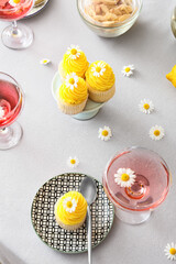 Stylish table setting with tasty cupcakes and chamomile flowers on light background