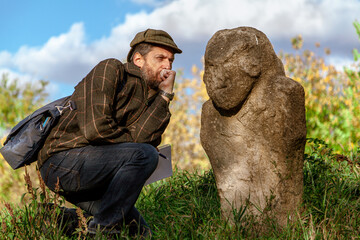 Scientist with beard examines stone sculpture on mound