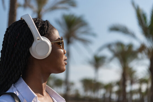 Young woman listen to music using wireless headphones while standing outdoors