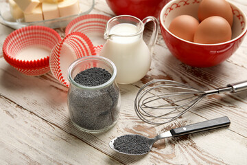 Jar with poppy seeds and ingredients for delicious muffins on wooden table