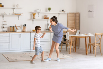 Young woman and her little son dancing and singing in kitchen