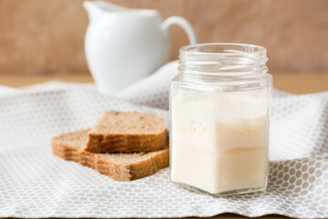 Jar with fresh sourdough and bread pieces on table