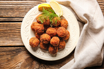 Plate with tasty cod cutlets with lemon on wooden background