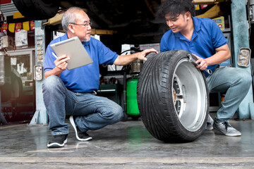 Two mechanic checking wheel at garage, car service technician check and repair customer car at automobile service, senior and young work together at vehicle repair service shop concept