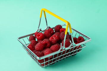 Red juicy raspberries in a shopping basket on a menthol background
