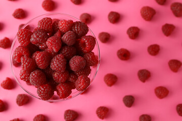 Red juicy raspberries in a glass on a pink background with raspberries, space for text
