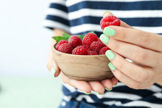 Woman holding wooden bowl with raspberries, cloce up