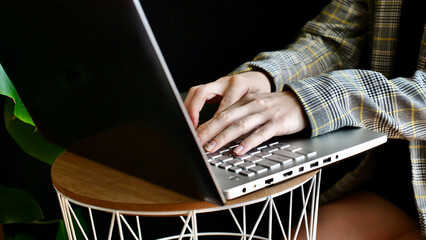 Close-up of woman's hands in a jacket typing on a laptop computer. The person works, studies at...
