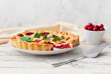 Plate with tasty cherry pie and spatula on light wooden background