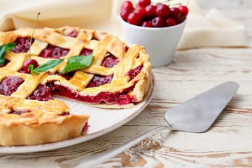 Plate with tasty cherry pie and spatula on light wooden background, closeup