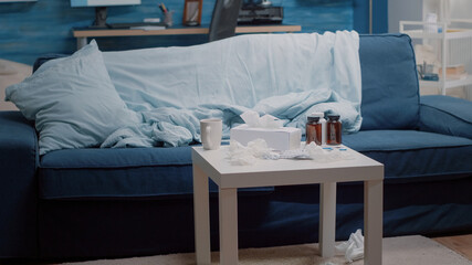 Empty living room with healthcare treatment on table for sick person. Nobody in place with medicine, bottles of pills, capsule tablets, tea and tissues used by adult with disease.