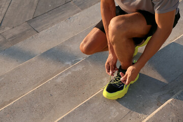 Sporty young man tying shoe laces outdoors