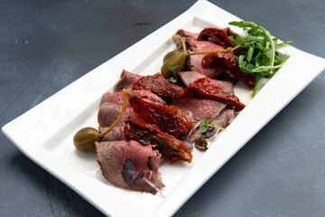 Snack. Meat, sun-dried tomatoes, capers and arugula in a plate.