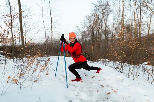 Female Runner Warming Up before Running in Woods in Winter. Sportswoman With Trekking Poles Stretching Before Trail Running On Cold Winter Day.