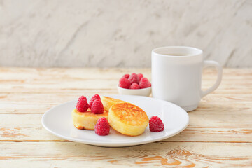 Plate with cottage cheese pancakes and raspberries on light wooden background