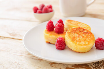 Plate with cottage cheese pancakes and raspberries on light wooden background
