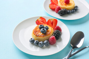 Plates with cottage cheese pancakes and berries on color background