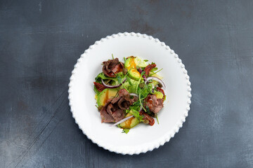 Salad with meat and avocado in a plate. On a gray background.