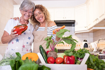 Senior mother hugging her daughter in the kitchen looking at the harvest on the table. Raw vegetables, healthy eating or diet