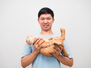 Young man holding orange cat and feeling heavy on white background