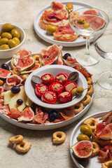 Appetisers and vermouth cocktail. Bruschetta, cold cuts of prosciutto, cheese, tuna fish stuffed mini bell peppers, taralli, olives, grapes and figs. Traditional italian aperitivo. Vertical image. - obrazy, fototapety, plakaty