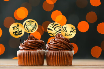 Tasty cupcakes for New Year 2022 celebration on table against blurred lights