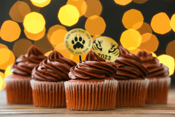 Tasty cupcakes for New Year 2022 celebration on table against blurred lights