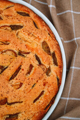 Apple pie charlotte in a white ceramic form on the background of a beige kitchen towel. Fresh fragrant pastries. Cozy autumn at home