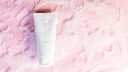 white cosmetic tube on a pink background with soap foam and bubbles. Face or body cleancer concept. Copy space