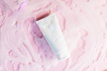 white cosmetic tube on a pink background with soap foam and bubbles. Face or body cleancer concept. Copy space