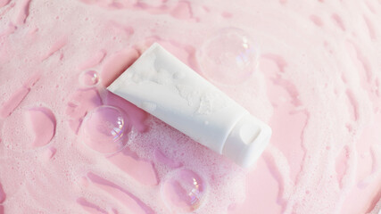 white cosmetic tube for shower gel, face or body cleancer on a pink background with soap foam and...