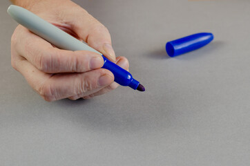 A hand holds a marker against a gray background. Adult male with a gray thick marker with blue cap....