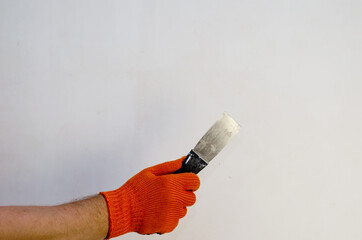 A hand in a red protective glove holds a metal spatula against the wall. A man with a hand-held...