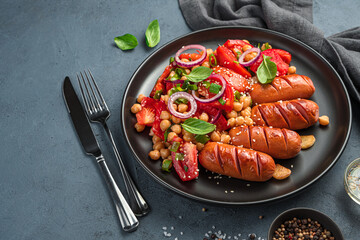 Dinner, a portion of chickpea salad and fried sausages on a dark background. Side view, copy space