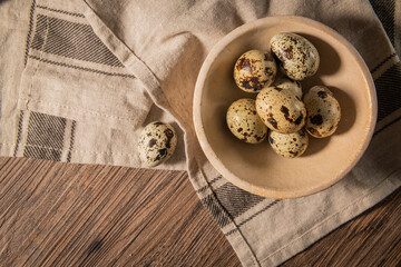Fototapeta na wymiar Fresh quail eggs on a ceramic bowl, brown wooden table. Raw quail eggs close-up on a culinary background. Concept of preparation for cooking