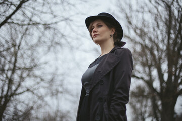 A middle-aged woman in a black raincoat and hat alone in the park. Autumn November wind. Gloomy rainy foggy weather. Loneliness sadness depression. Despair. Mental health lifestyle. Melancholy mood