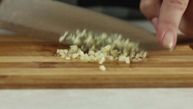 chop garlic with a knife on a wooden cutting board at kitchen table close-up