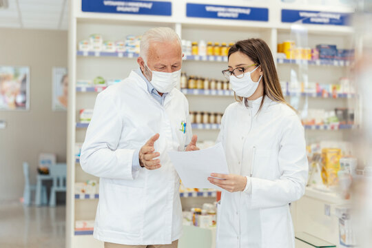 Colleague advice. Documentation and paper work in pharmacies during corona virus. A senior pharmacist explains the documentation in the pharmacy to a young pharmacist They wear uniforms and face masks